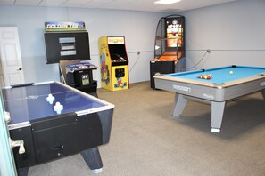Sala de lazer com duas mesas de pebolim, uma mesa de bilhar e máquinas de jogos eletrônicos.