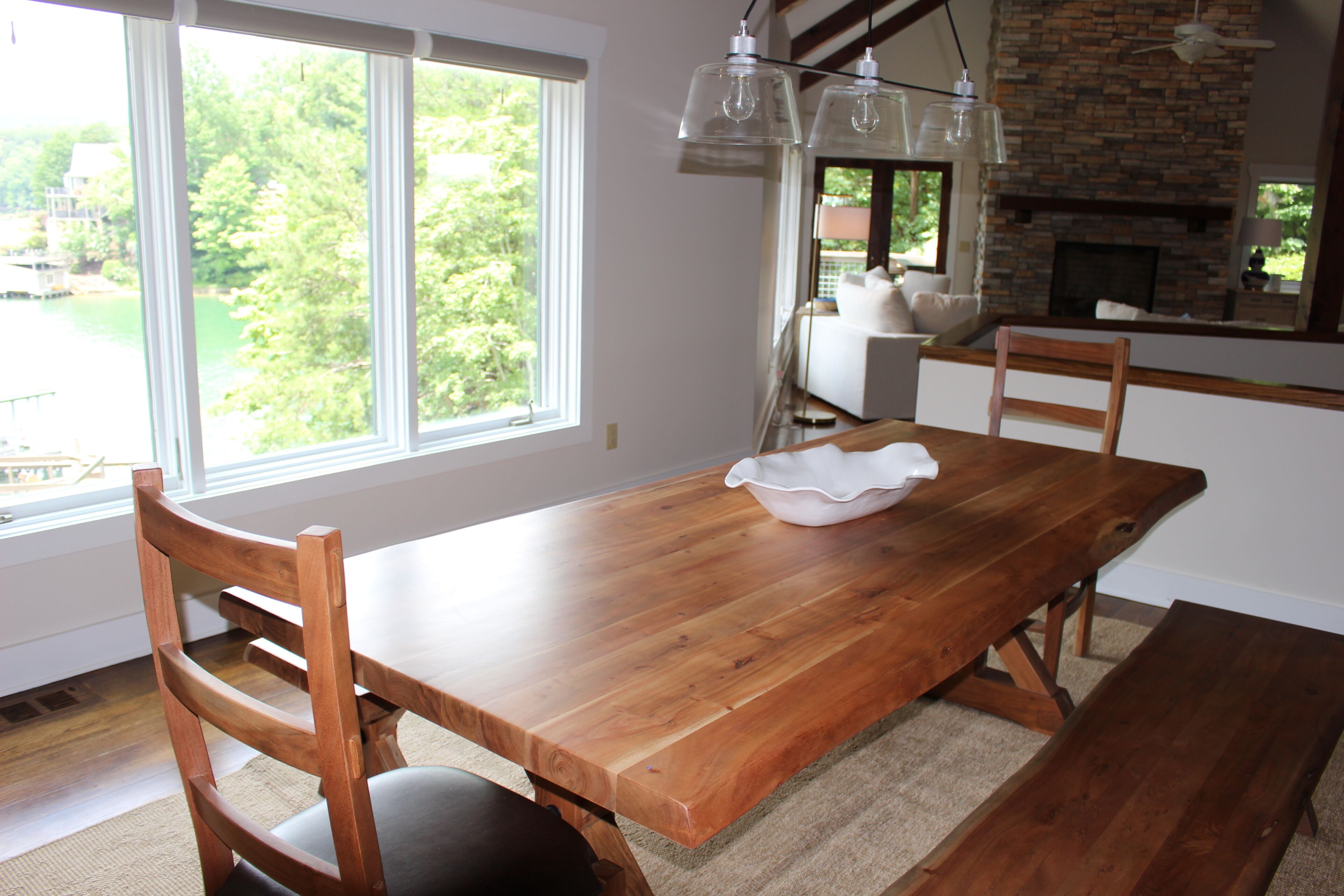 Een eetgedeelte met een houten tafel, stoelen, een schaal en uitzicht op groen.