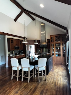 A modern kitchen with wooden cabinets, a central island with seating, and a large stove. - Vista Cove Lake Lure- Private Cove & Game Room (Lake Lure)