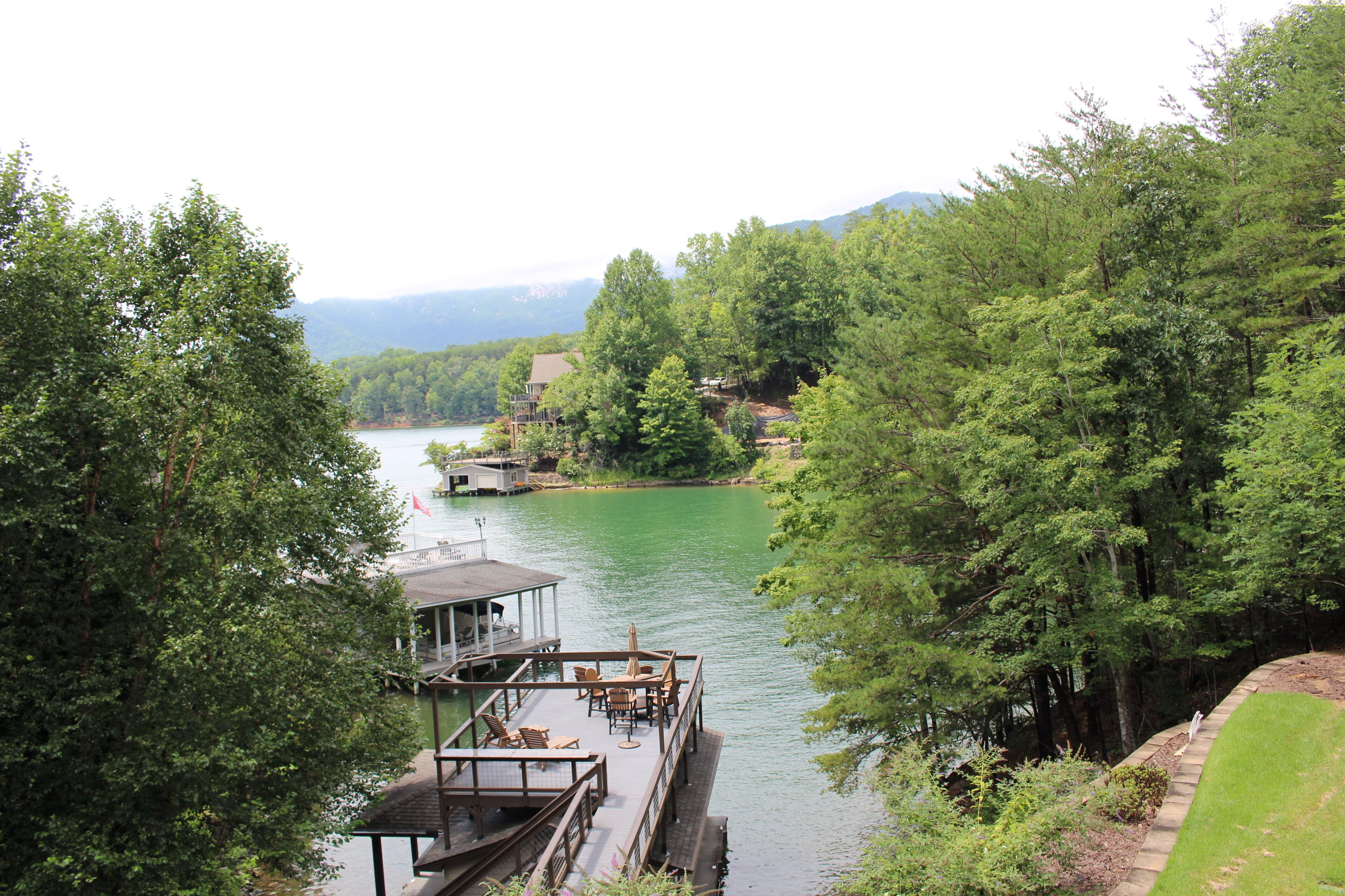 A riverside dock with a covered seating area and a small building, surrounded by dense greenery and hills in the background.