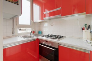 A kitchen with red cabinets, a gas stove, a sink, and a window. - Cozy 45 sqm flat, perfect for 3 people, located on the 5th floor of a building with elevator.The property is situated in the Calvairate district, a residential area characterized by the green spaces of Piazza Insubria & Viale Molise.The Porta Romana dist (Milan)