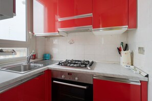 A kitchen with red cabinets, a stainless steel sink, and a gas stove. - Cozy 45 sqm flat, perfect for 3 people, located on the 5th floor of a building with elevator.The property is situated in the Calvairate district, a residential area characterized by the green spaces of Piazza Insubria & Viale Molise.The Porta Romana dist (Milan)
