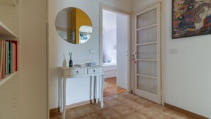 A hallway with a white console table, a round mirror, a door with glass panels, and a colorful abstract painting on the wall. - Cozy 45 sqm flat, perfect for 3 people, located on the 5th floor of a building with elevator.The property is situated in the Calvairate district, a residential area characterized by the green spaces of Piazza Insubria & Viale Molise.The Porta Romana dist (Milan)