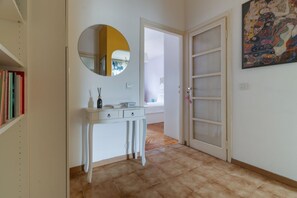 A hallway with a white console table, a round mirror, a door with glass panels, and a colorful abstract painting on the wall. - Cozy 45 sqm flat, perfect for 3 people, located on the 5th floor of a building with elevator.The property is situated in the Calvairate district, a residential area characterized by the green spaces of Piazza Insubria & Viale Molise.The Porta Romana dist (Milan)