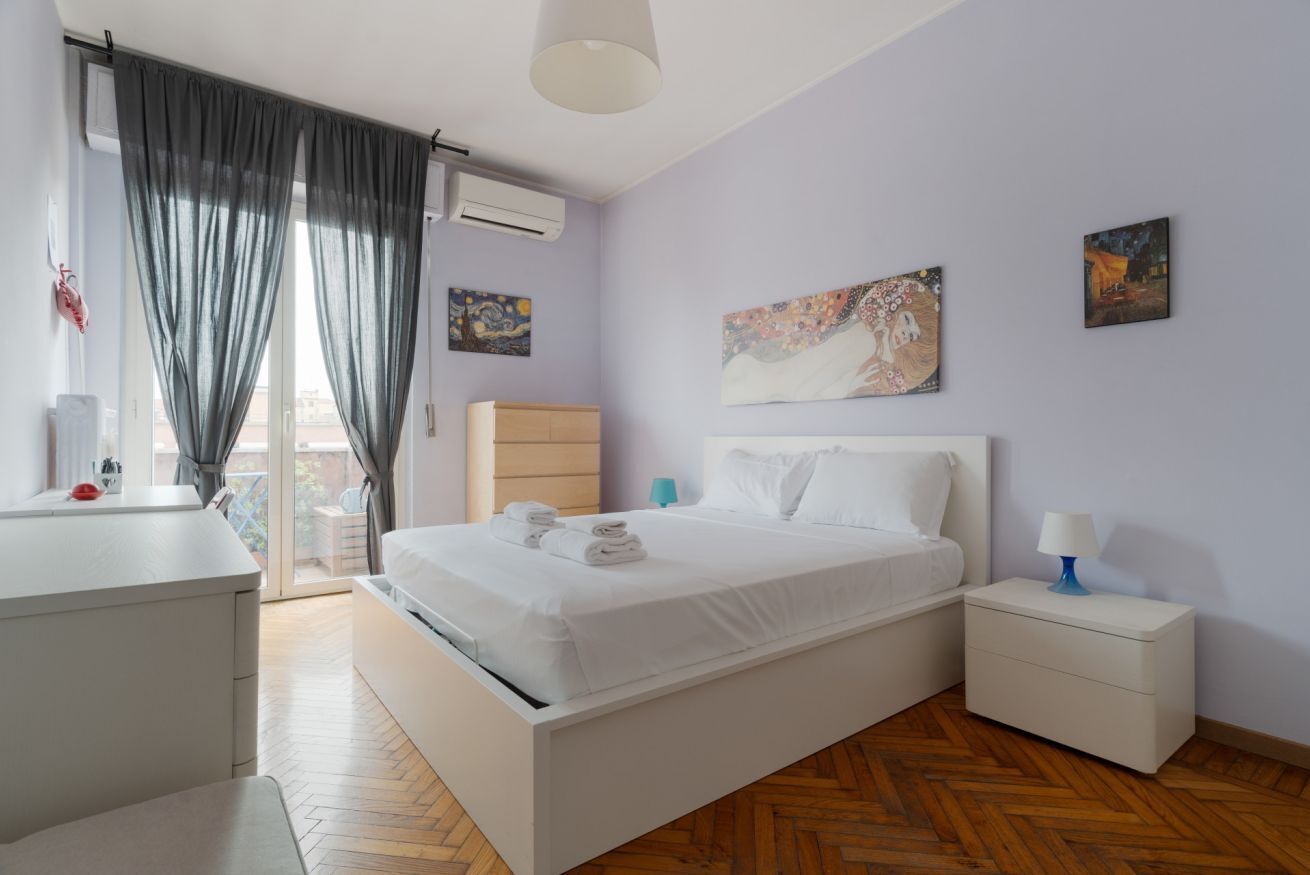 Ein modernes Schlafzimmer mit Bett, Nachttischen, Schreibtisch und einem Fenster mit Vorhängen.