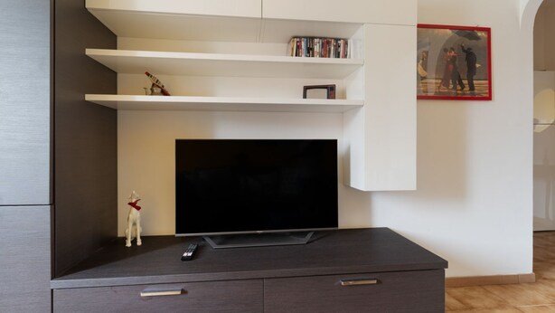 A modern living room with a flat-screen TV, a small dog figurine, and a bookshelf with books and a framed picture. - Cozy 45 sqm flat, perfect for 3 people, located on the 5th floor of a building with elevator.The property is situated in the Calvairate district, a residential area characterized by the green spaces of Piazza Insubria & Viale Molise.The Porta Romana dist (Milan)