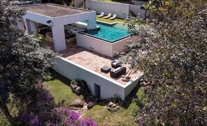 Un área de piscina moderna al aire libre, con piscina rectangular, sillones de descanso y un patio con asientos.