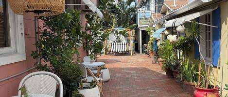 A paved walkway with outdoor seating, potted plants, and a clear sky.