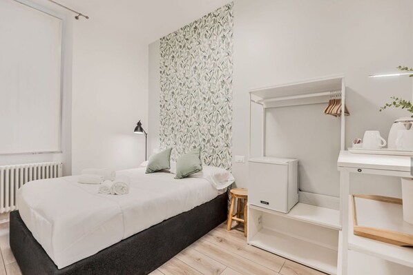 Un dormitorio moderno con una cama, un taburete pequeño, un armario blanco y un radiador.