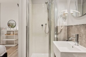 Ein modernes Badezimmer mit einer Glaskabine zur Dusche, einem weißen Waschbecken und einem Spiegel.