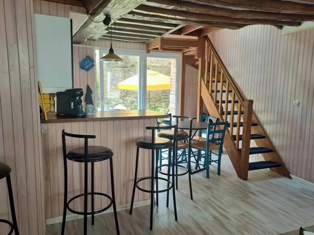 A kitchen with a wooden bar counter, stools, and a staircase.