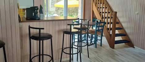A kitchen with a wooden bar counter, stools, and a staircase.