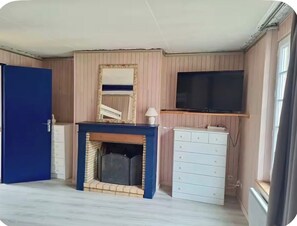 A room with a fireplace, a television mounted on the wall, a blue door, and a white dresser. - Duplex with a garden in downtown Honfleur (Honfleur)