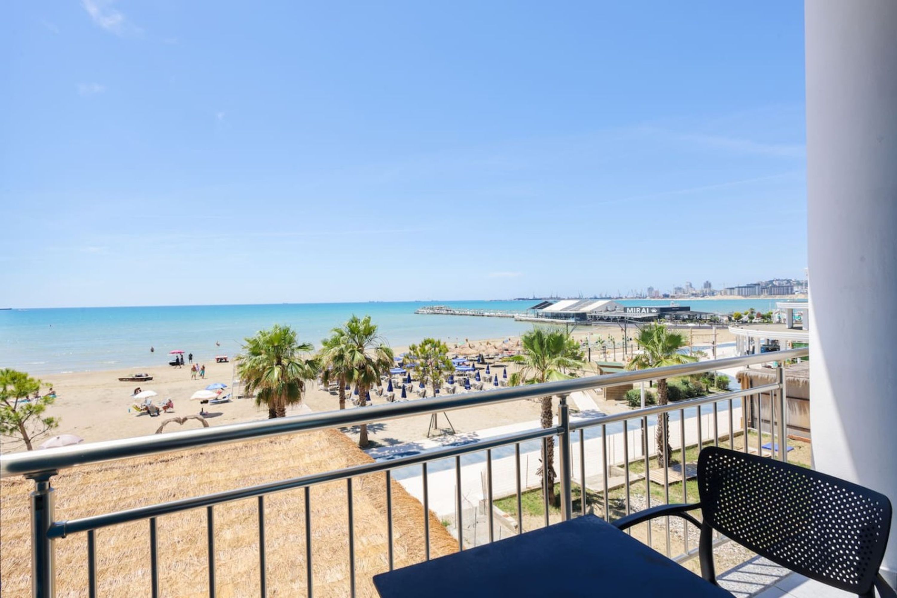 Een balkon met uitzicht op een strand, palmbomen en een stadsbeeld in de verte.