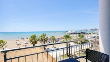 Een balkon met uitzicht op een strand, palmbomen en een stadsbeeld in de verte.