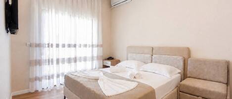 A hotel room with a bed, a bedside table, a chair, and an air conditioning unit.