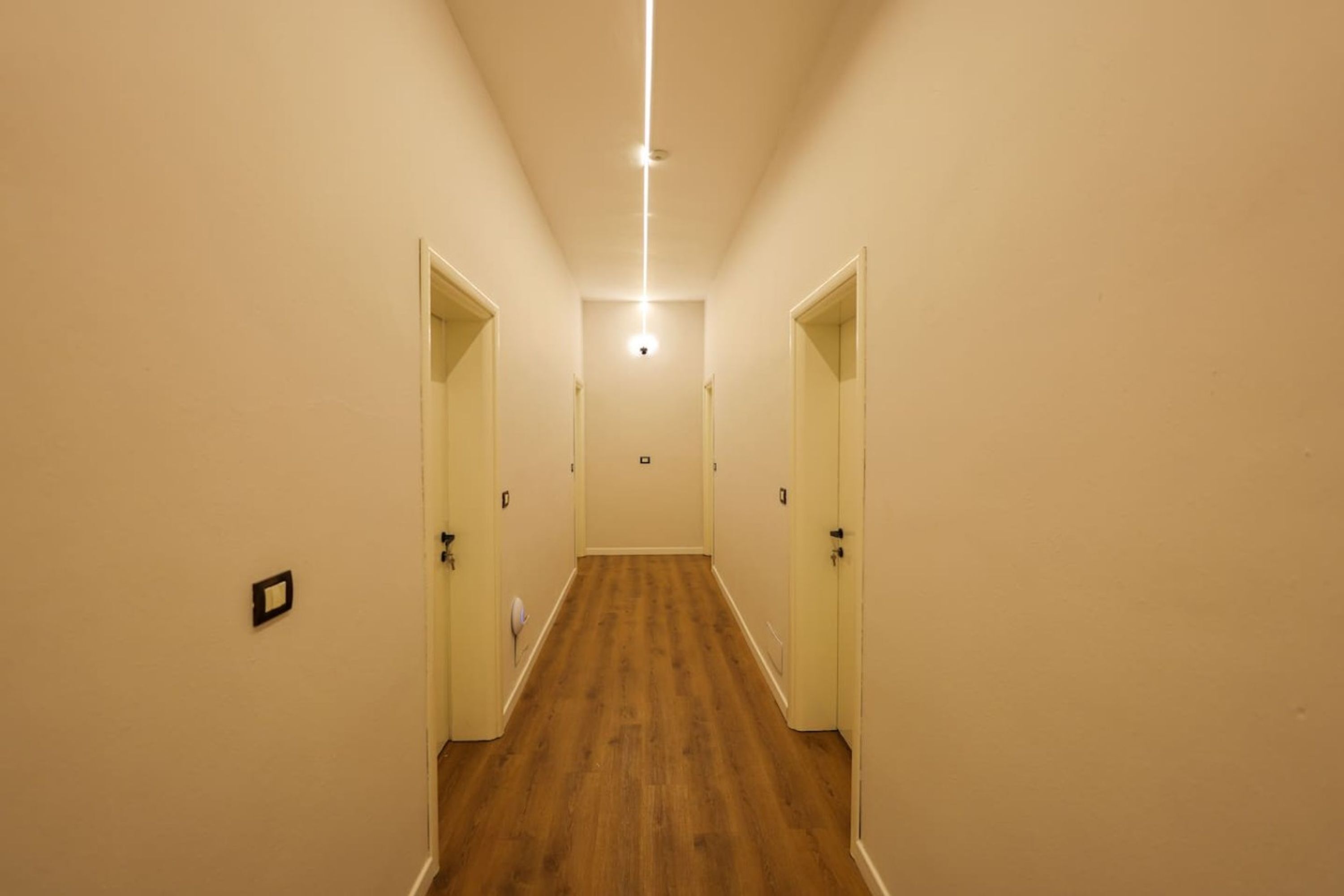 A narrow hallway with wooden flooring and white walls, leading to a door at the end.