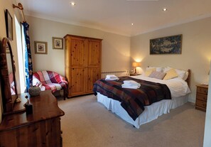 A bedroom with a bed, a wooden wardrobe, a chair, and a painting on the wall. - Curlew Cottage (Crianlarich)