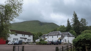 A rural setting with white buildings, a gravel driveway, and a mountain in the background.