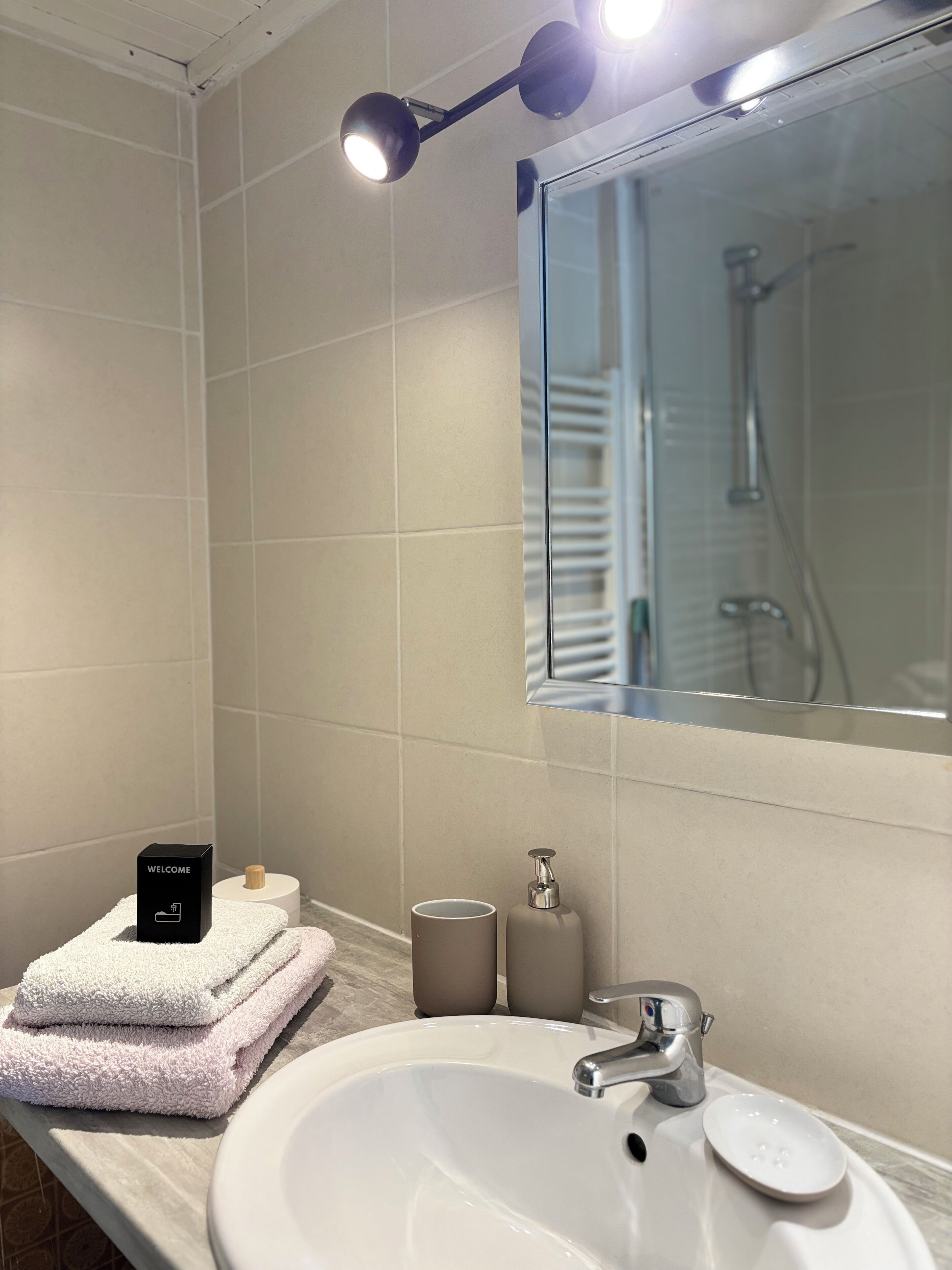 A bathroom with a white sink, a mirror, a towel rack, and a welcome sign.