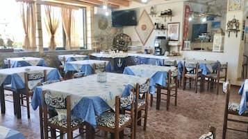 A dining area with multiple tables and chairs, a television mounted on the wall, and various decorative items.