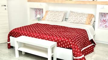 A bed with a red patterned bedspread, white pillows, and a white bench in front of it.