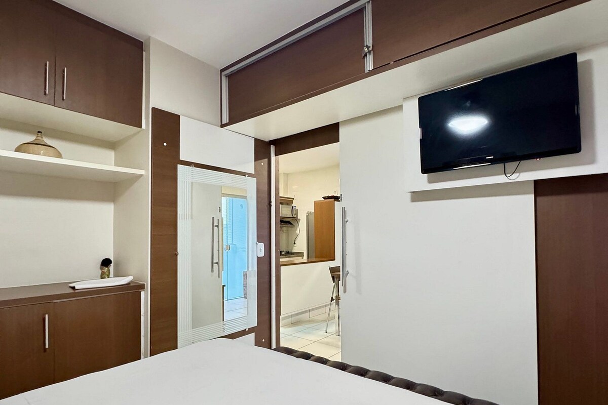 A hotel room with a bed, a television mounted on the wall, and a wardrobe.
