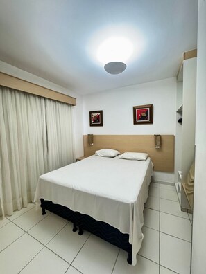 A hotel room with a bed, curtains, a headboard, two wall-mounted picture frames, and a mirror. - Pontal do Lago Flat Residence, Aproveite Dias Incriveis em Familia as Margens do Lago Corumba (Caldas Novas)