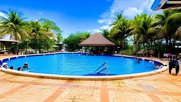 A swimming pool with a tiled deck, surrounded by palm trees and a gazebo.