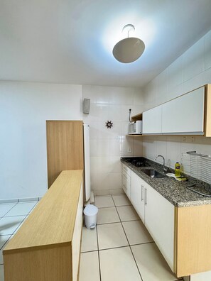 A modern kitchen with white cabinets, a granite countertop, a built-in microwave, and a hanging light fixture. - Pontal do Lago Flat Residence, Aproveite Dias Incriveis em Familia as Margens do Lago Corumba (Caldas Novas)