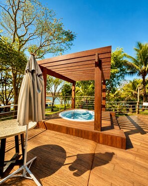 Una terraza de madera con un jacuzzi, una mesa y un espacio de estar techado.