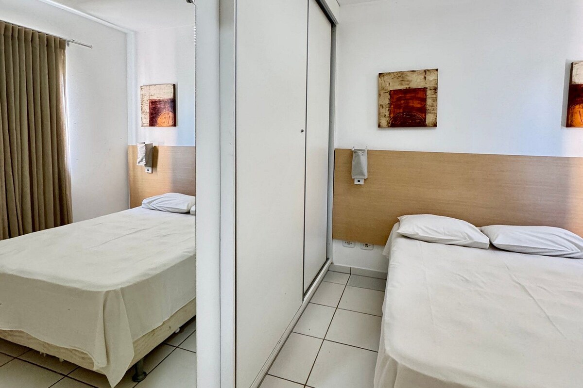 A hotel room with two beds, a mirror, a wooden headboard, and artwork on the walls.