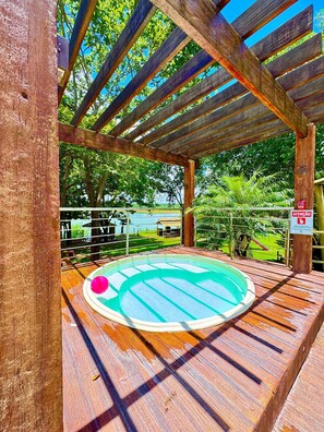 Una terraza de madera con un jacuzzi, rodeada por una barandilla metálica y árboles.