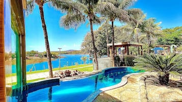 Piscina com design curvo, cercada por palmeiras e vista para um corpo de água.