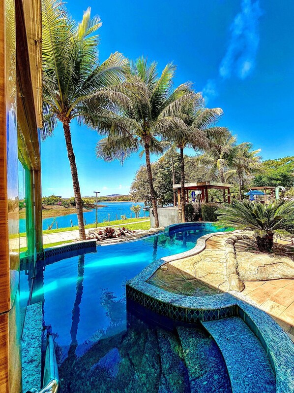 A swimming pool with a curved design, surrounded by palm trees and a view of a body of water.