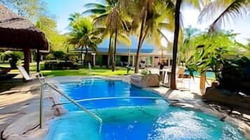 A swimming pool with clear blue water, surrounded by palm trees and a thatched-roof structure.