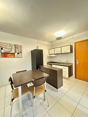 A modern kitchen with white cabinets, a dining table with chairs, and a painting on the wall. - Pontal do Lago Flat Residence, Aproveite Dias Incriveis em Familia as Margens do Lago Corumba (Caldas Novas)