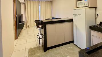 A compact kitchen with a refrigerator, microwave, and a small bar area with stools.