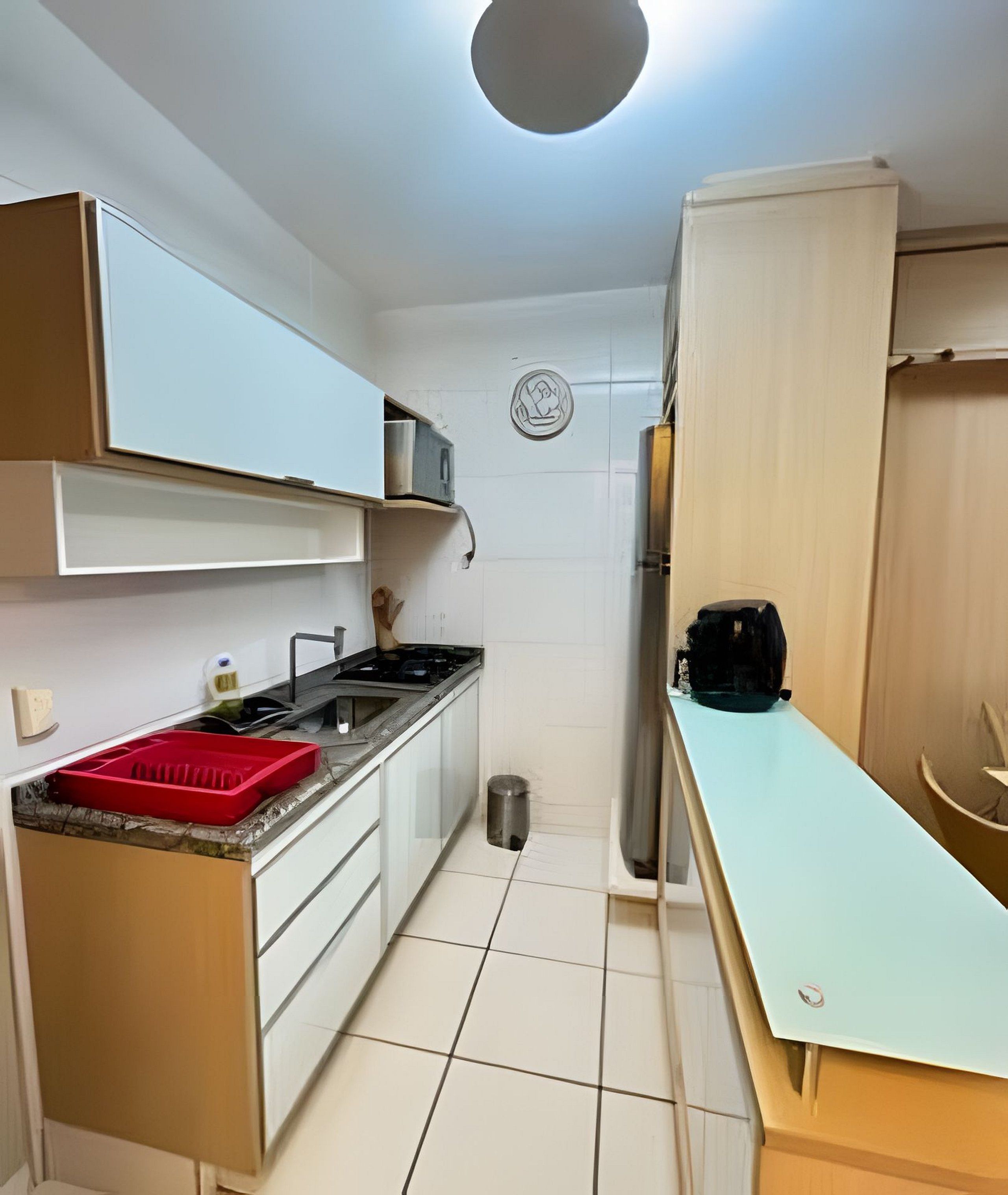 Uma cozinha compacta com armários brancos, uma pia de aço inoxidável e um escorredor de louça vermelho.