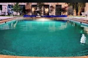 Une piscine aux eaux claires, recouverte d’une bâche bleue sur le pourtour, est entourée d’un bâtiment doté de nombreuses fenêtres et portes.