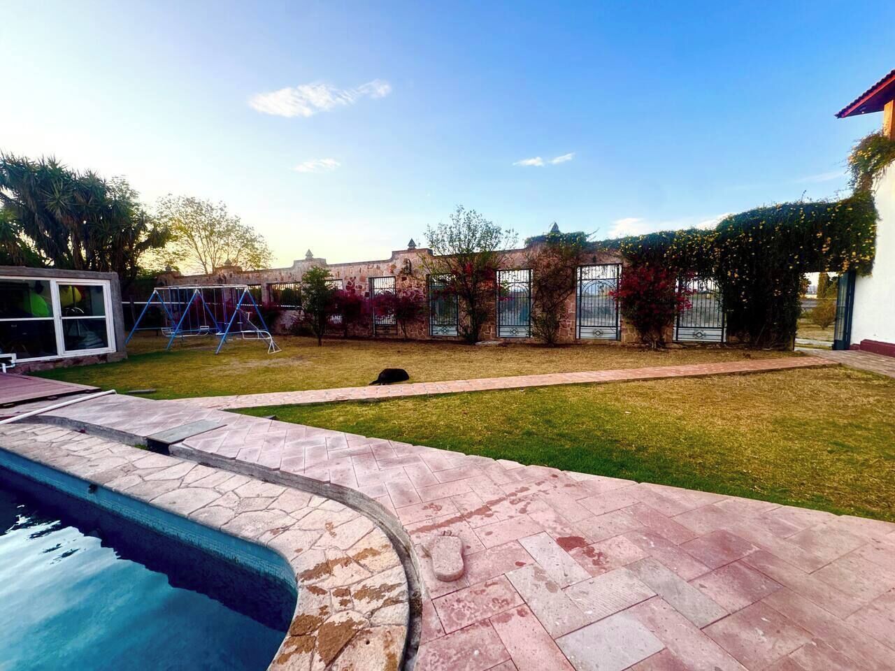 A swimming pool with a stone deck, a grassy lawn, and a building with a brick facade in the background.