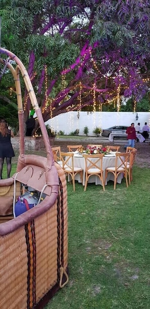 Un espace extérieur aménagé pour les repas, avec des meubles en osier et un grand arbre aux feuilles violettes.