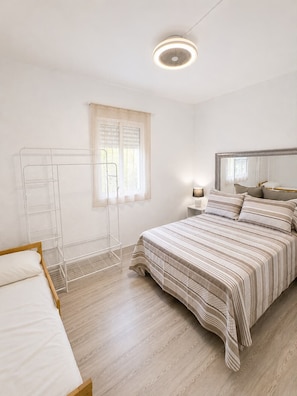Ein Schlafzimmer mit Bett, Nachttisch, Lampe, einem Fenster mit Jalousien und einer Deckenleuchte.
