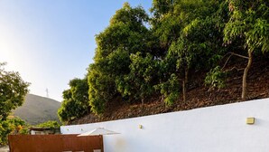 A swimming pool with a white wall and a wooden deck with chairs. - Casa Jimena con Piscina Privada (Torrox)
