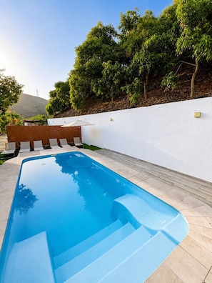 Ein Swimmingpool mit weißer Wand und einer Holzterrasse mit Stühlen.