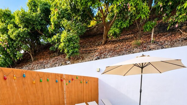 A backyard with artificial grass, white lounge chairs, a wooden fence, and a string of colorful lights. - Casa Jimena con Piscina Privada (Torrox)