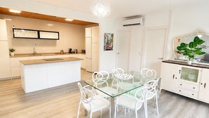 A modern kitchen with white cabinetry, a central island, and a dining area with a glass table and white chairs. - Casa Jimena con Piscina Privada (Torrox)