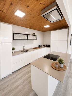 A modern kitchen with white cabinetry, a wooden ceiling, and a central island with a built-in stove. - Casa Jimena con Piscina Privada (Torrox)
