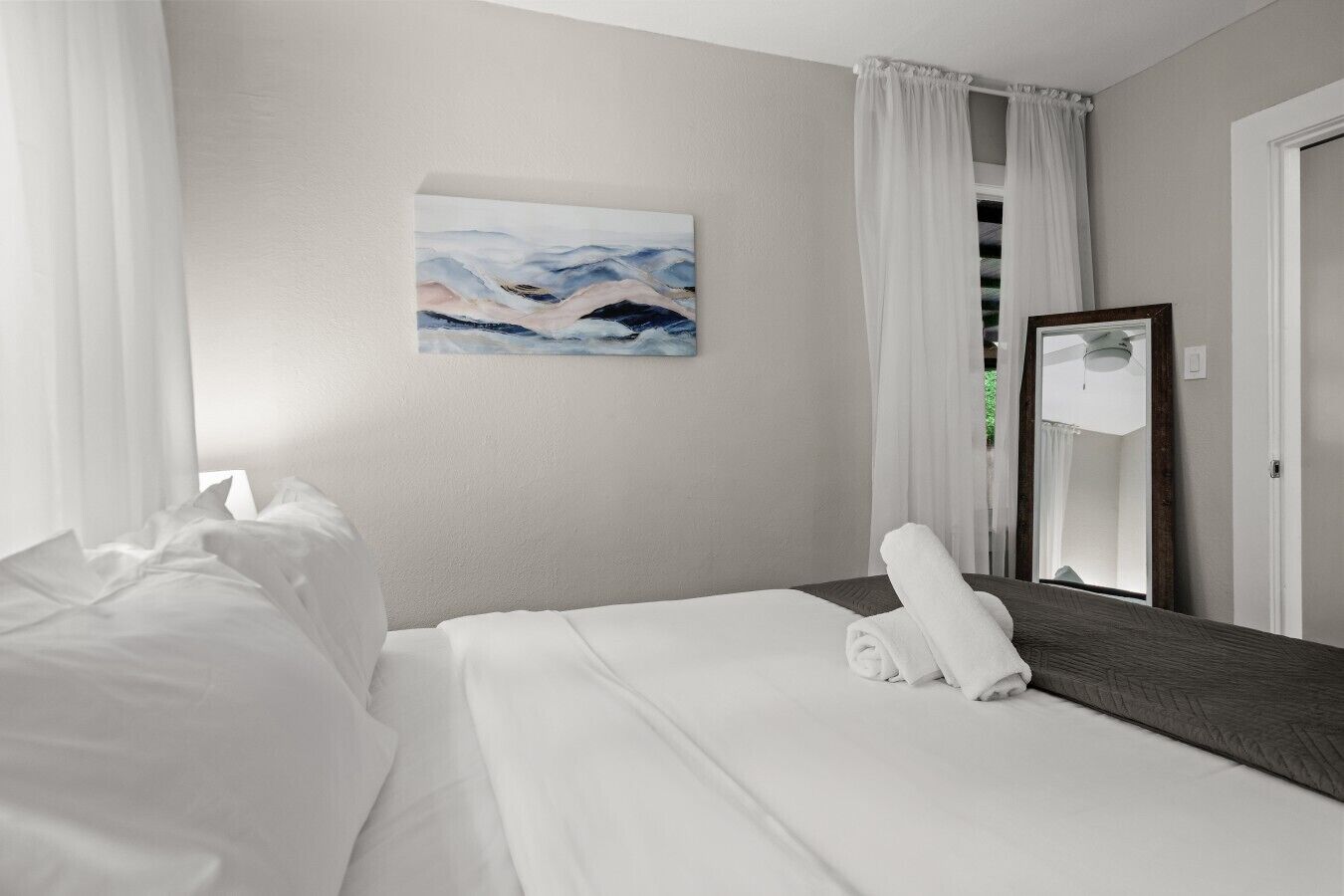 Een hotelkamer met een net opgemaakt bed, een grote spiegel en een schilderij aan de muur.