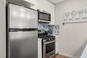 Eine kompakte Küche mit einem Edelstahl-Kühlschrank, einer Mikrowelle, einem Gasherd und einem Backofen.